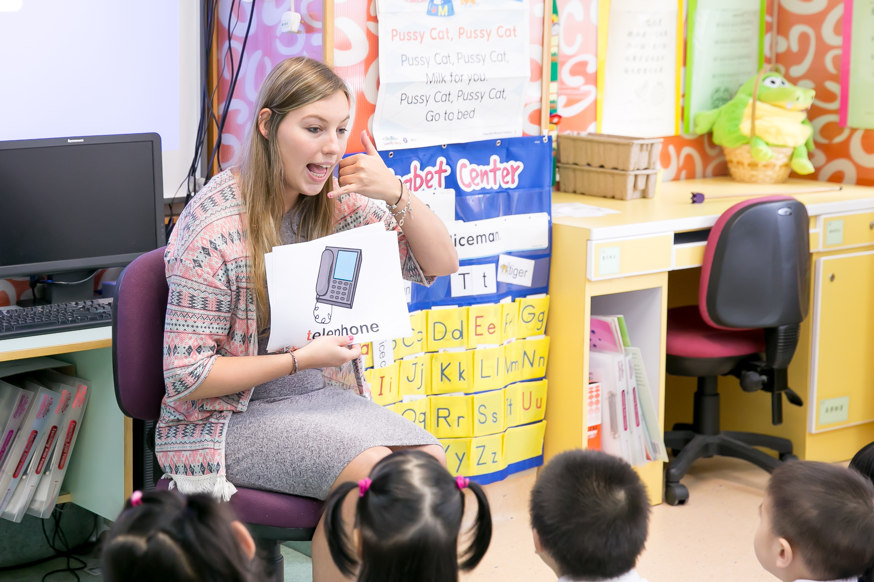 a TEFL teacher in the classroom explaining children the word telephone